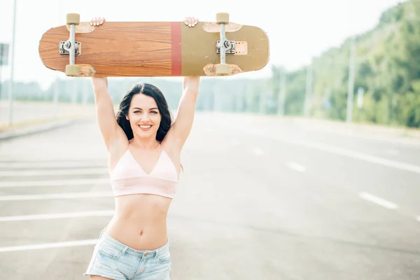 어린 소녀는 화창 한 날 어깨에 스케이트보드를 메고 서 있다 — 스톡 사진