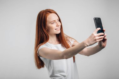 Beyaz arka planda duran kızıl saçlı kadın. Kenara bakınca özçekim yap.