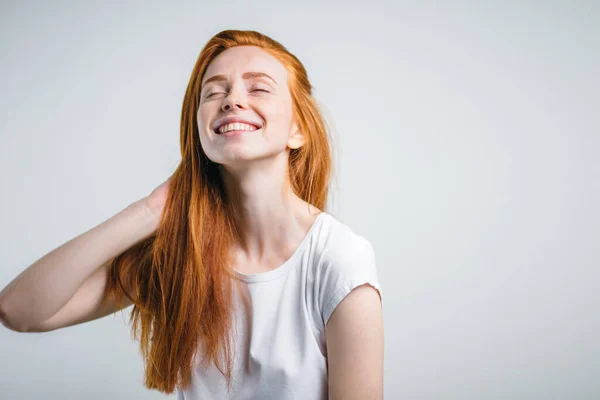 Девушка с веснушками, улыбающаяся с закрытыми глазами, трогающая свои рыжие волосы — стоковое фото