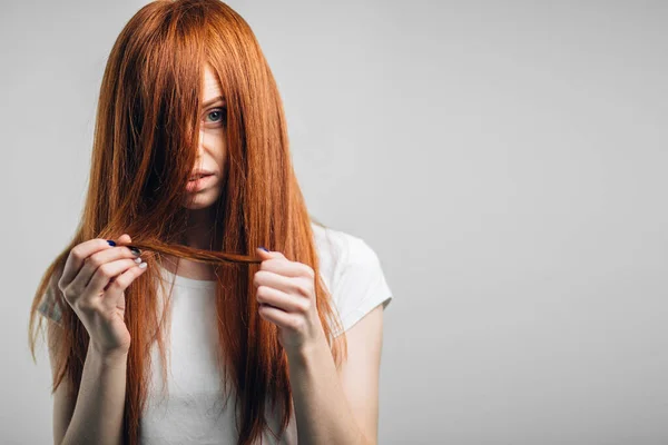 Triste ragazza rossa che tiene i capelli danneggiati guardando la fotocamera. — Foto Stock