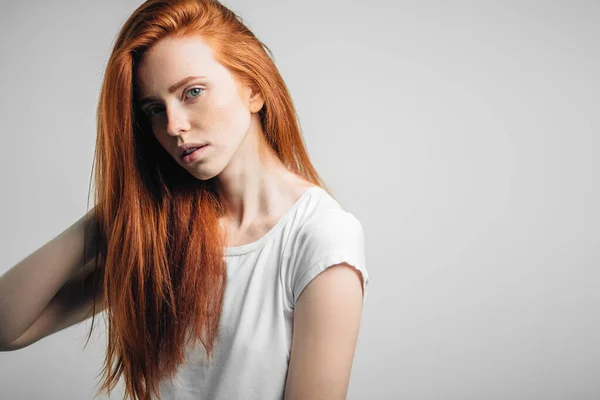 Ung söt rödhårig flicka med fräknar tittar på kameran ler rörande hår — Stockfoto