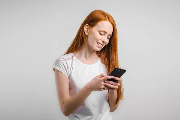 Рыжая девушка с чистой веснушки кожа с помощью смартфона и смс и улыбка. — стоковое фото