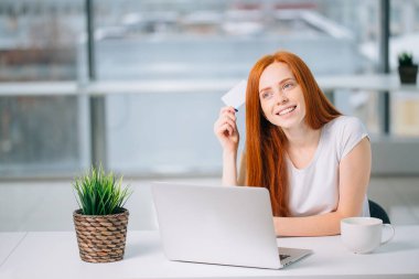 Elinde kredi kartıyla ne alacağına karar veren mutlu kızıl saçlı müşteri.