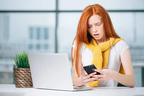 Boldog vörös hajú lány sms üzenetet küld a barátjának, miközben a modern irodában dolgozik — Stock Fotó
