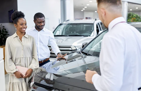Schönes schwarzes Paar hört Berater im Autohaus aufmerksam zu — Stockfoto