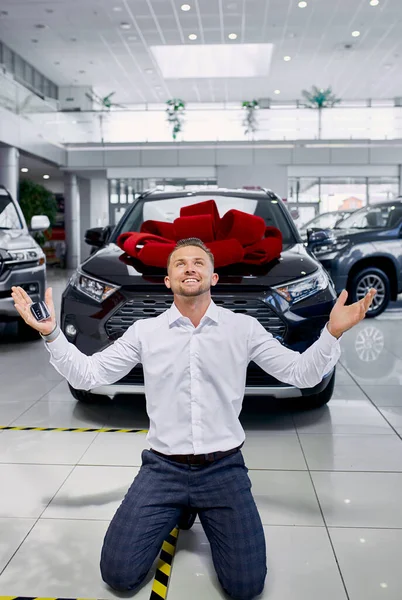 Felice bell'uomo caucasico in piedi sulle ginocchia davanti alla sua auto fresca appena comprata — Foto Stock