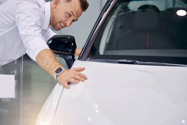 Attraente cliente uomo si trova accanto a bianco auto di lusso in concessionaria — Foto Stock