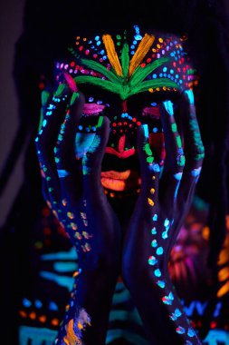 Ultraviyole vücut sanatındaki Afrikalı adam yüzüne dokunuyor.