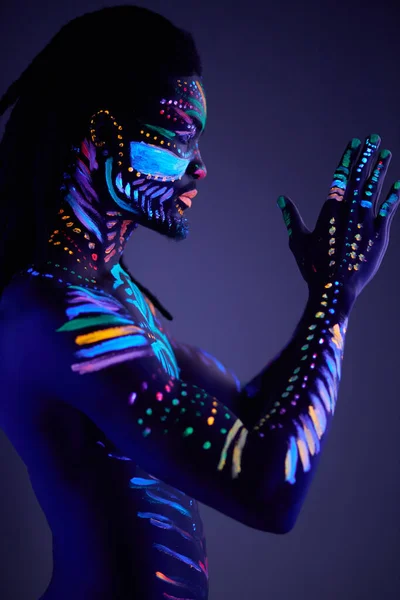 Muscular young man in bright blacklight bodyart glowing in darkness — Stock Photo, Image