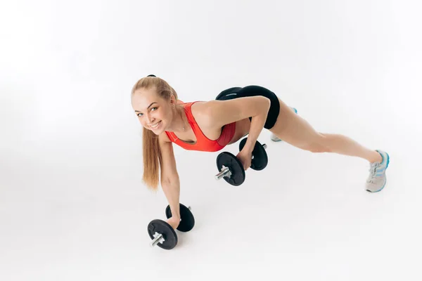 Mujer deportiva haciendo flexiones con mancuernas en el gimnasio — Foto de Stock