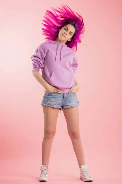 ピンクの背景の上にカメラを見て飛行紫色の髪を持つ美しいファッションの女の子. — ストック写真
