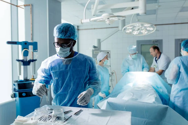 Afrika man i mask och kopp tar kirurgiska instrument — Stockfoto