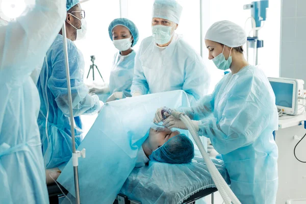 Careful clever doctors adjusting oxygen mask on patient in hospital room — Stock Photo, Image