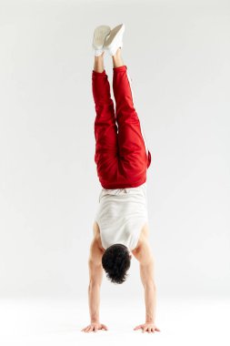 Kırmızı eşofmanlı genç adam beyaz arka planda amuda kalkıyor.