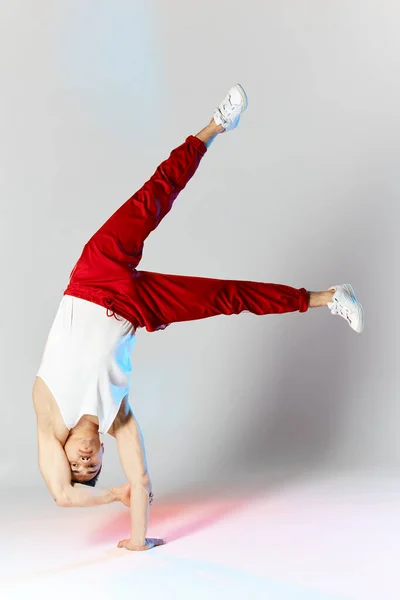 Hombre joven en pantalones de chándal rojos haciendo un soporte de mano en las manos sobre fondo blanco —  Fotos de Stock