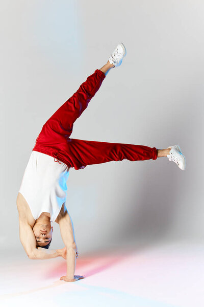 Young man in red sweatpants doing a handstand on hands on white background