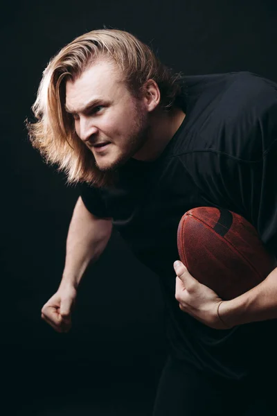 Entschlossener American-Football-Spieler in Aktion isoliert auf schwarzem Hintergrund — Stockfoto