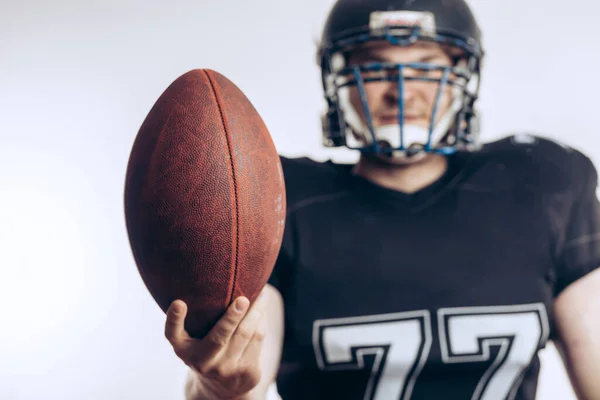Musculoso futbolista americano en uniforme protector y casco sosteniendo pelota —  Fotos de Stock