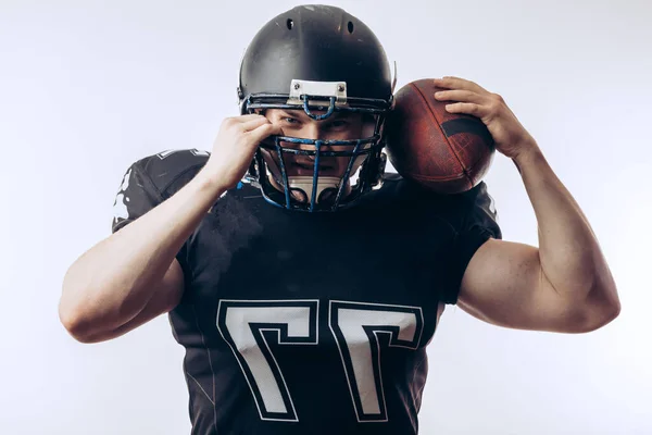 Musculoso futbolista americano en uniforme protector y casco sosteniendo pelota — Foto de Stock