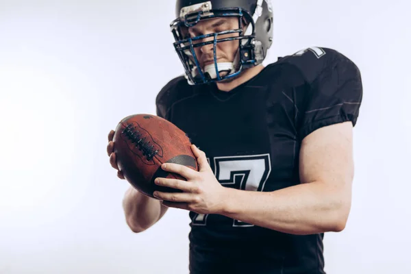 Мускулистый американский футболист в защитной форме и шлеме, держащий мяч — стоковое фото