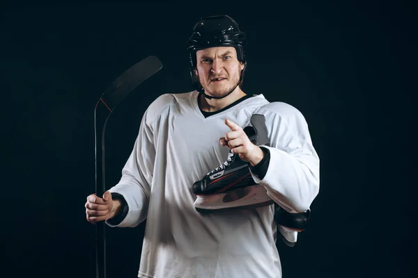 Jugador de hockey seguro mirando a la cámara con el patín en la mano. Aislado en negro. —  Fotos de Stock
