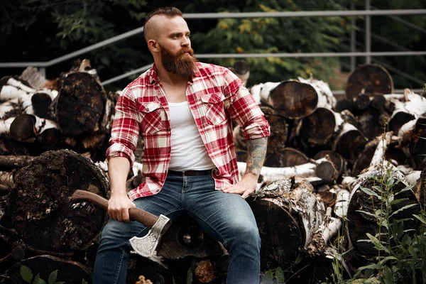 Man sitting on firewoods. Woodcutter with axe resting after work — Stock Photo, Image