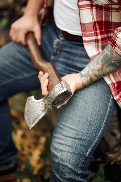 Close up man in checkered shirt sitting on logs and holding axe — Stock Photo, Image