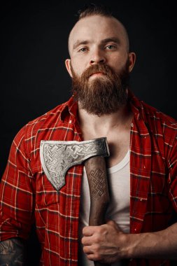 Göğsünde baltası olan sakallı bir erkek stüdyoda poz veriyor.