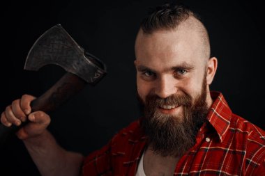 Elinde baltayla gülümseyen sakallı adam siyah arka plandaki kameraya bakıyor.