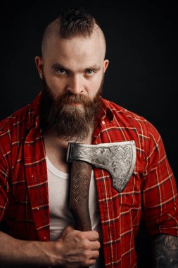 Göğsünde baltası olan sakallı bir erkek stüdyoda poz veriyor.