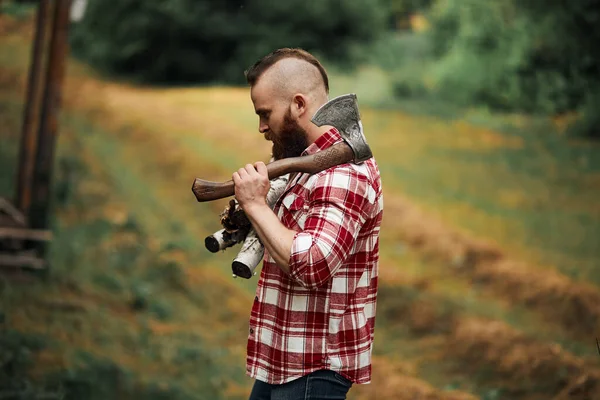 Homem barbudo com lenha e com machado no ombro — Fotografia de Stock