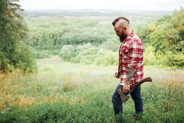 Man med yxa, skägg rutig skjorta, skogshuggare, natur bakgrundspromenader i skogen — Stockfoto