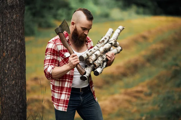 Bearded Man with firewoods and with axe on shoulder — Stock Photo, Image