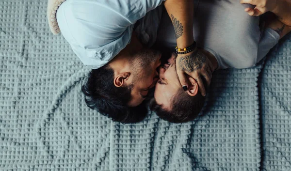 Bonito homem sonolento com cerda beijando boa noite parceiro masculino deitado na cama — Fotografia de Stock