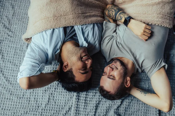 Bonito homem sonolento com cerda beijando boa noite parceiro masculino deitado na cama — Fotografia de Stock