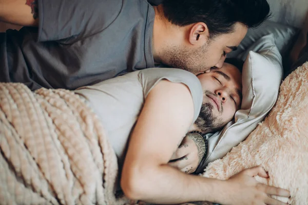 Zwei hübsche schwule Männer, nackt im Bett zusammen kuscheln und lächeln einer von ihnen hat sichtbare Pecs und definierte Bauchmuskeln — Stockfoto