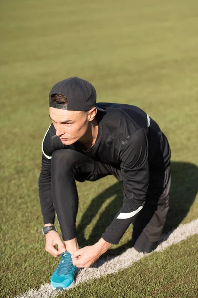 Slim fit guy sitting on the grass and lacing up shoes — Stock Photo, Image