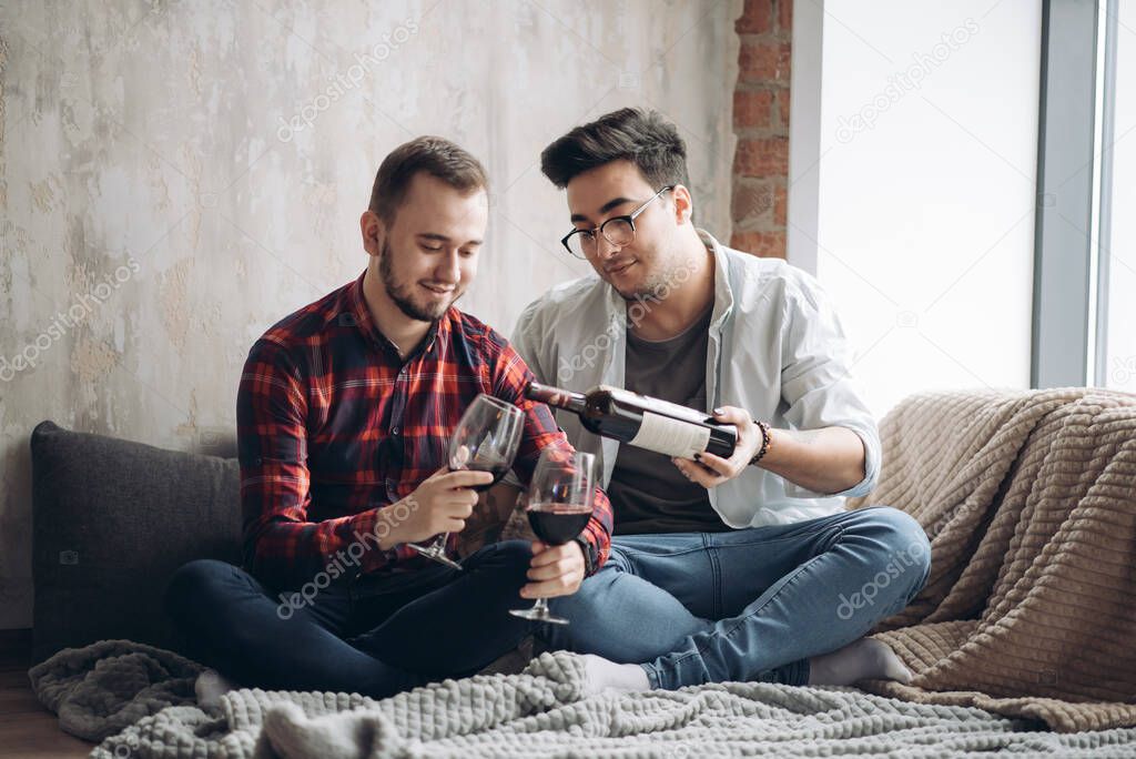 Laughing male gay couple drinking wine and preparing a meal