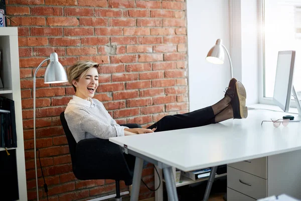 beautiful blond girl with legs on the table is singing thee sons at workplace