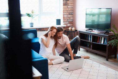 Genç evli çift yerde dizüstü bilgisayar kullanarak dinleniyor.