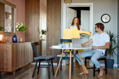 Kızıl saçlı kadın kocasının kıyafetini sevip sevmediği sorusuyla ilgileniyor.