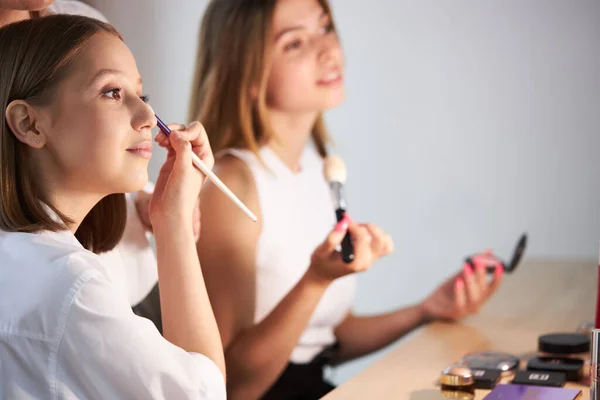 Meninas atraentes aplicando cosméticos no rosto, fazendo maquiagem em si mesmos — Fotografia de Stock