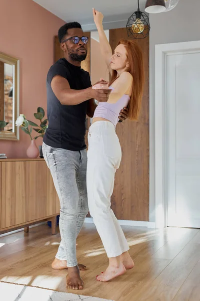 Schöne junge multiethnische Paare tanzen im Wohnzimmer — Stockfoto