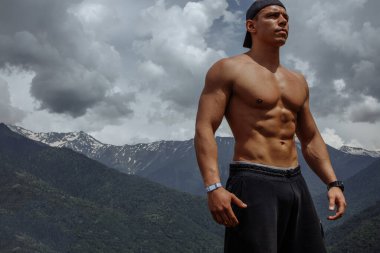 Dağlarda poz veren vücut geliştirici. Yakışıklı güçlü adam kaslarını gösteriyor..