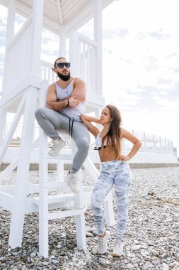 Genç çift, çakıl taşlı plajda dinlenirken kulaklıkla müzik dinliyor.