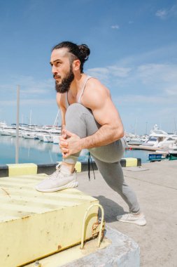 Sahilde durup suya bakarken elini uzatan bir sporcunun arka görüntüsü.