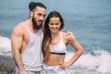 Yaz sabahı kumsalda sarılan bir çift ve arka planda deniz kölesi.