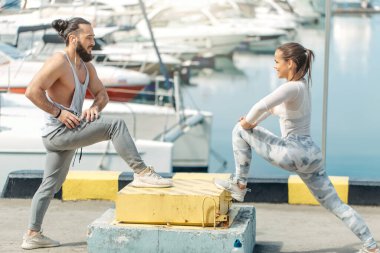Genç ve güzel bir çift okyanus rıhtımında esneme egzersizleri yapıyor.