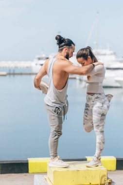 Genç ve güzel bir çift okyanus rıhtımında esneme egzersizleri yapıyor.