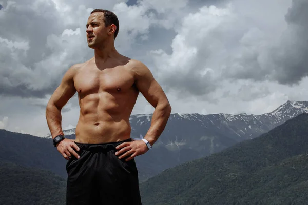 Fisiculturista posando nas montanhas. Bonito homem forte mostrando seus músculos. — Fotografia de Stock